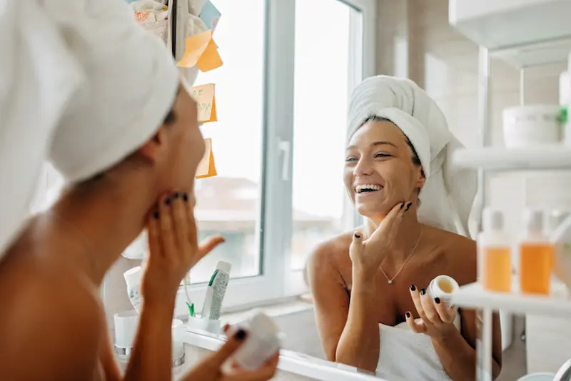 bella mujer realizando rutina matutina de skin care en su baño